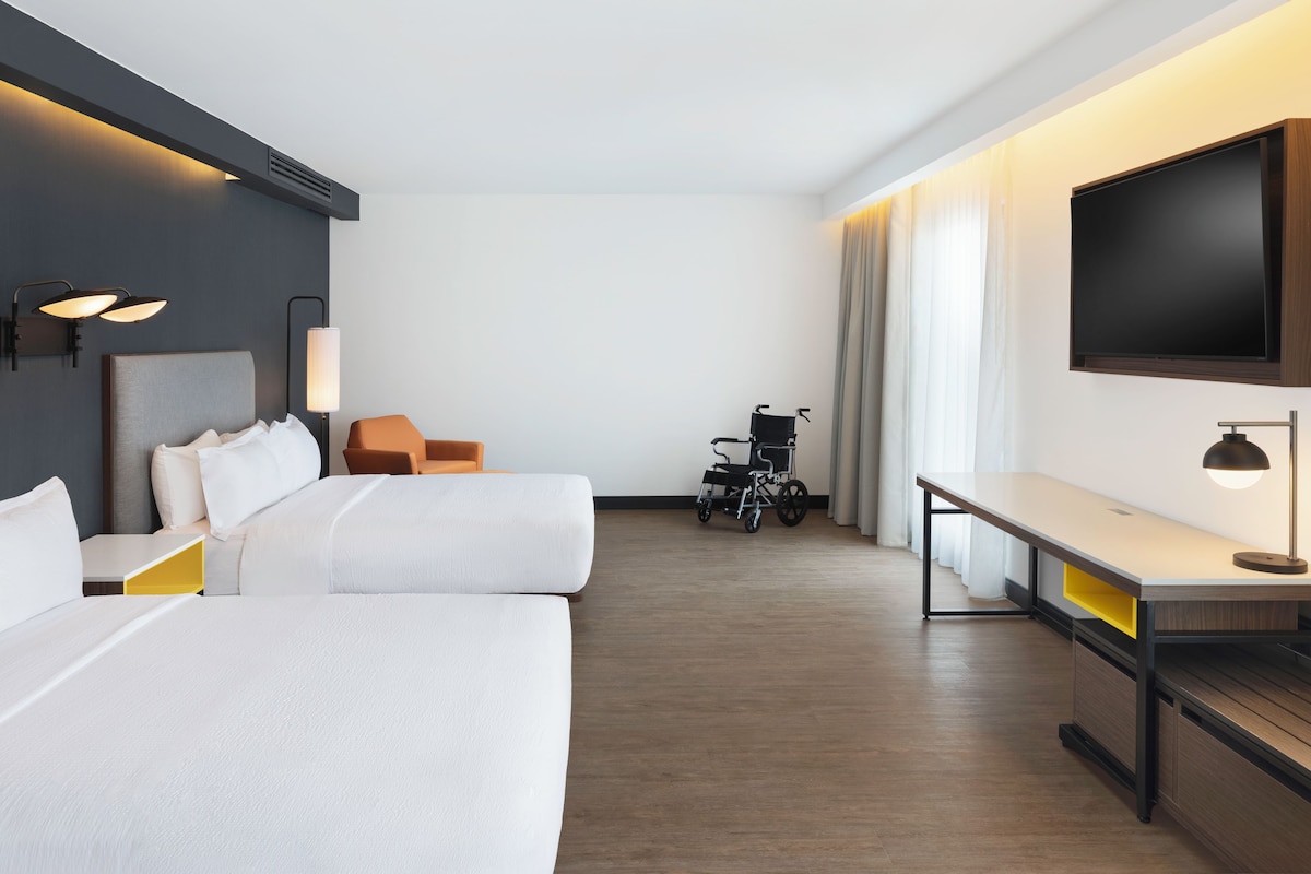 Une chambre d’hôtel avec deux lits, un bureau, une télévision et un fauteuil roulant.