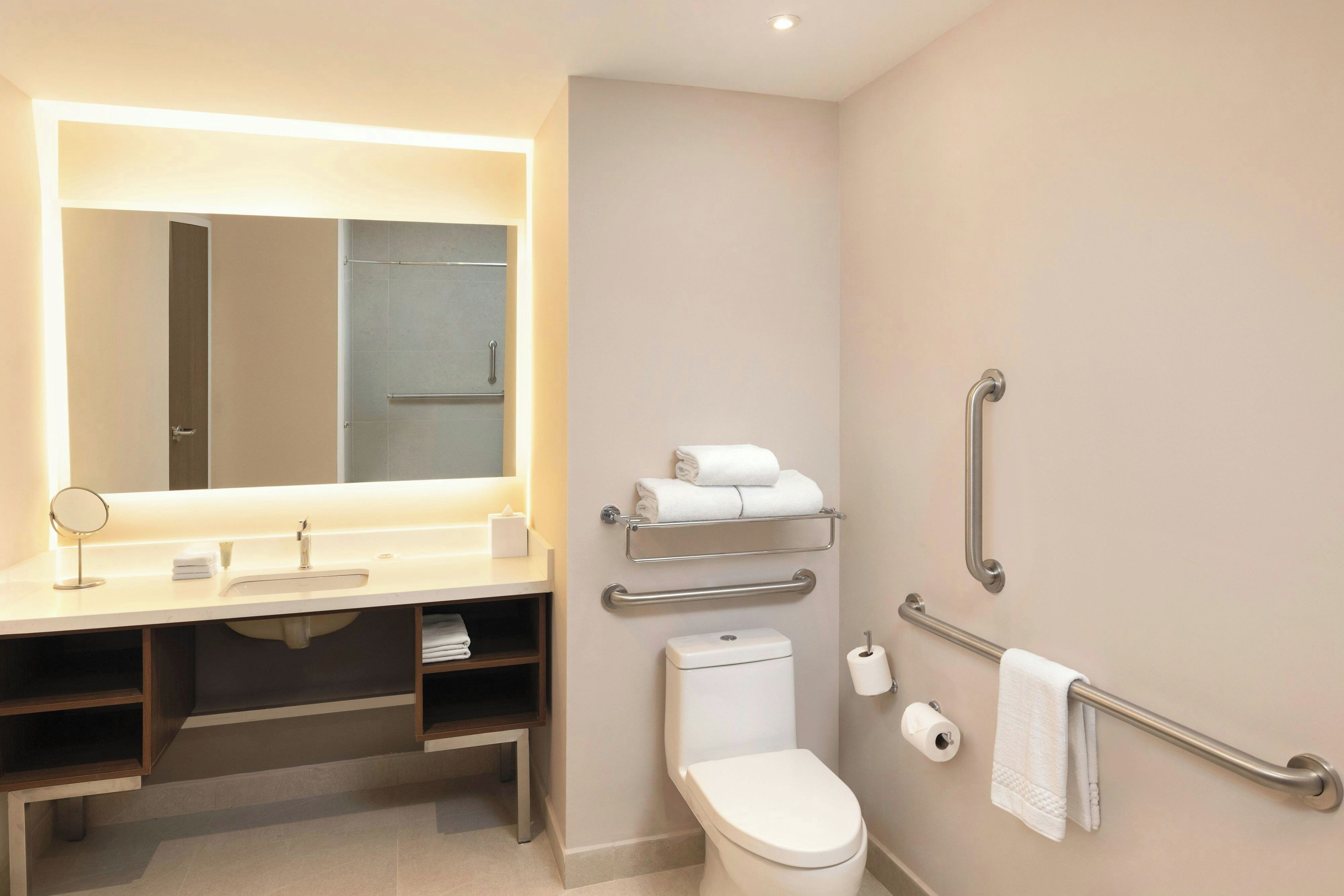 Un baño moderno con tocador, espejo, inodoro y barras de apoyo.