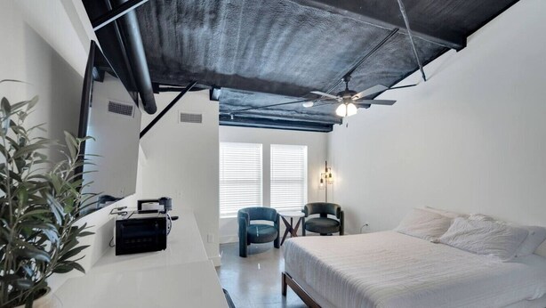 Une chambre moderne avec un lit, un bureau, une chaise et un ventilateur de plafond.