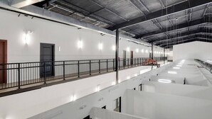 Un intérieur spacieux de style industriel, avec de hauts plafonds, des conduits apparents et un long couloir doté d’une rambarde noire.