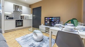 A modern kitchen with white cabinets, a built-in oven, and a glass dining table set for four. - Leeds Central Cosy 1BD Flat 10 mins to Station! (Leeds)