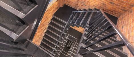 A spiral staircase with metal railings, brick walls, and a carpeted floor.