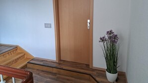 A wooden door with a handle, a small potted plant with purple flowers, and a wooden staircase with a handrail. - NEW! Apartment Calbe an der Saale (Calbe)