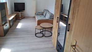 A room with a sofa, two small round tables, a television on a stand, and a wardrobe with a mirror. - NEW! Apartment Calbe an der Saale (Calbe)