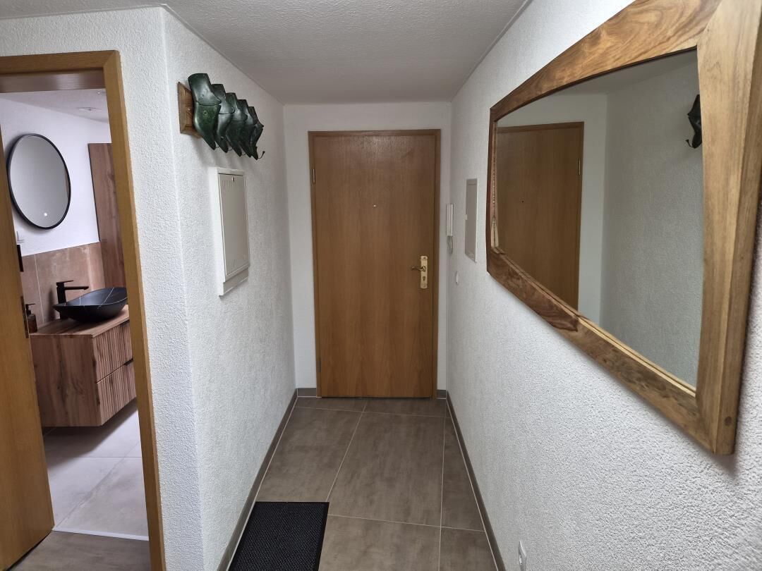 Um corredor com porta de madeira, espelho e luminária fixada na parede.