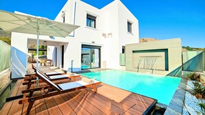 Ein modernes Haus mit Swimmingpool, Holzterrasse und Liegestühlen.
