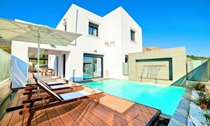 Ein modernes Haus mit Swimmingpool, Holzterrasse und Liegestühlen.
