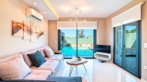 Ein modernes Wohnzimmer mit Sofa, Fernseher, Blick auf einen Pool und Kunstwerken an der Wand.