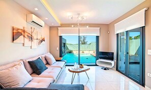 Ein modernes Wohnzimmer mit Sofa, Fernseher, Blick auf einen Pool und Kunstwerken an der Wand.