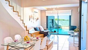 Ein modernes Wohnzimmer mit einem Glastisch, einer Couch, einem Fernseher und Blick auf einen Swimmingpool.