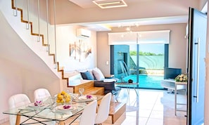Ein modernes Wohnzimmer mit einem Glastisch, einer Couch, einem Fernseher und Blick auf einen Swimmingpool.