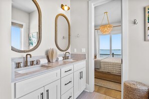 Ein Badezimmer mit einem großen Spiegel, einem Waschbecken mit Marmorplatte und Blick auf ein Schlafzimmer mit Bett und Balkon.