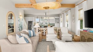 Ein modernes Wohnzimmer mit Sofa, Sesseln, einem Essbereich und einem Fernseher.