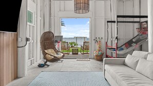 Ein Zimmer mit einer Couch, einem Korbsessel, einer Hängematte, einem Fernseher und Blick ins Freie.