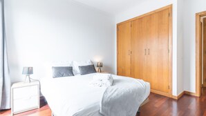 A bedroom with a bed, bedside tables, a wardrobe, and a nightstand. - Apartamento Calçada Encantada by Atlantic Holiday (Caniço)