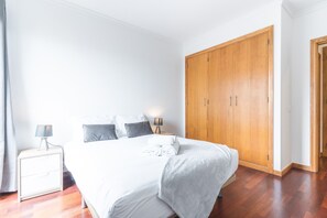 A bedroom with a bed, bedside tables, a wardrobe, and a nightstand. - Apartamento Calçada Encantada by Atlantic Holiday (Caniço)