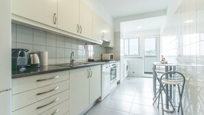 A modern kitchen with white cabinets, a stove, and a sink. There is a dining area with a table and chairs. - Apartamento Calçada Encantada by Atlantic Holiday (Caniço)