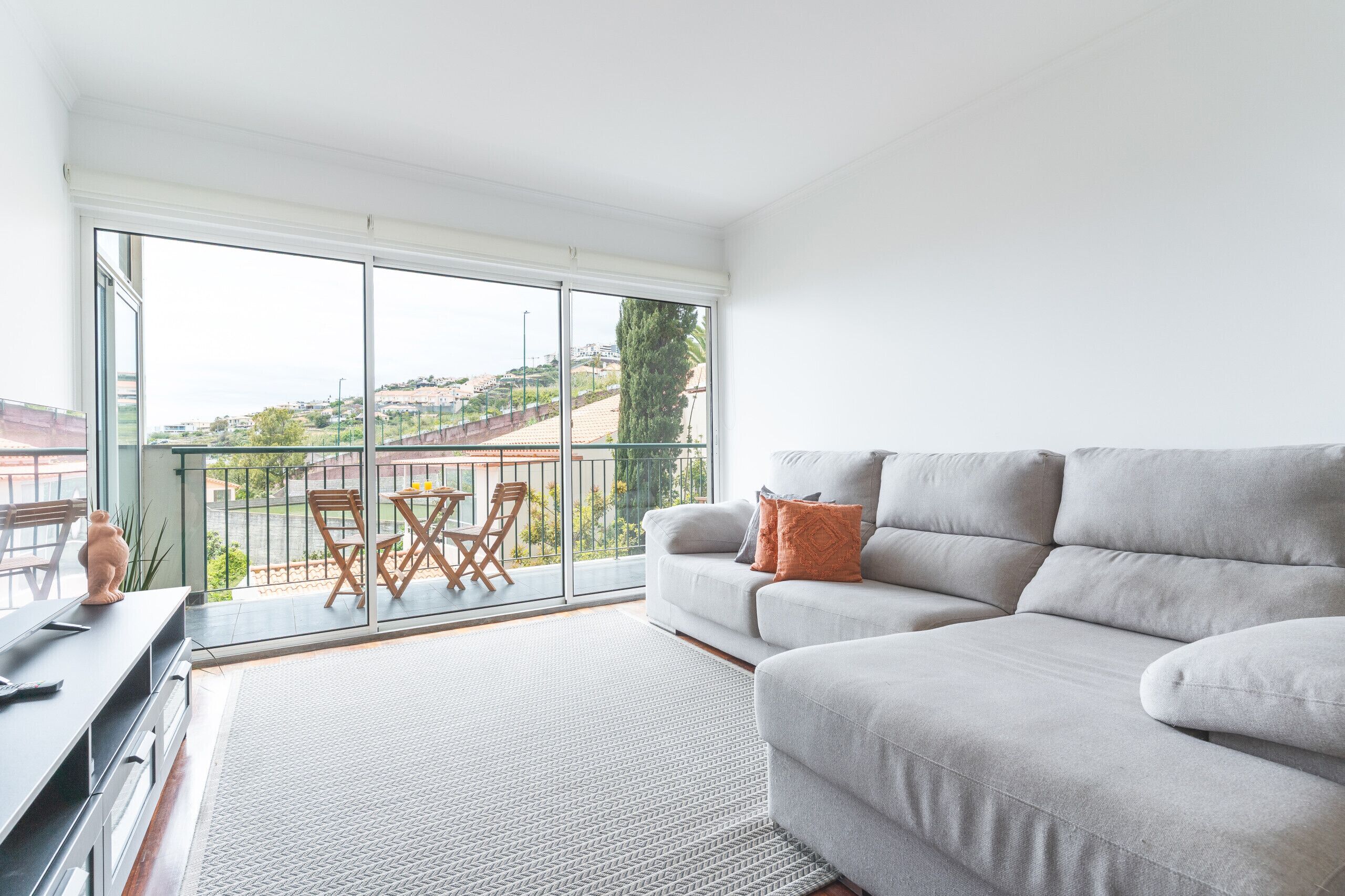 Ein modernes Wohnzimmer mit einem grauen Sofa, einem kleinen Tisch und einem Balkon mit Blick.