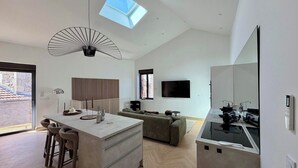 A modern kitchen with a central island, a dining area with bar stools, a living space with a sofa, and a large mirror. - Le Chai - Gervans (Gervans)
