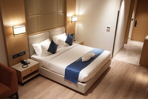 Una habitación de hotel moderna con una cama grande, lámparas de noche, un teléfono en la mesita y suelo de madera.
