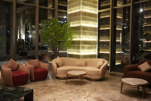 A modern interior with a curved sofa, red armchairs, a small round table, and a large illuminated column. - MEGHDOOT RESORT PRIME (Ujjain)