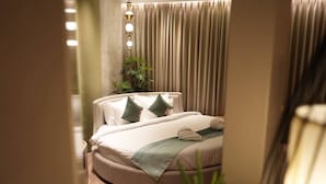 Ett hotellrum med en säng, kuddar, ett sängbord, en lampa och en gardin.