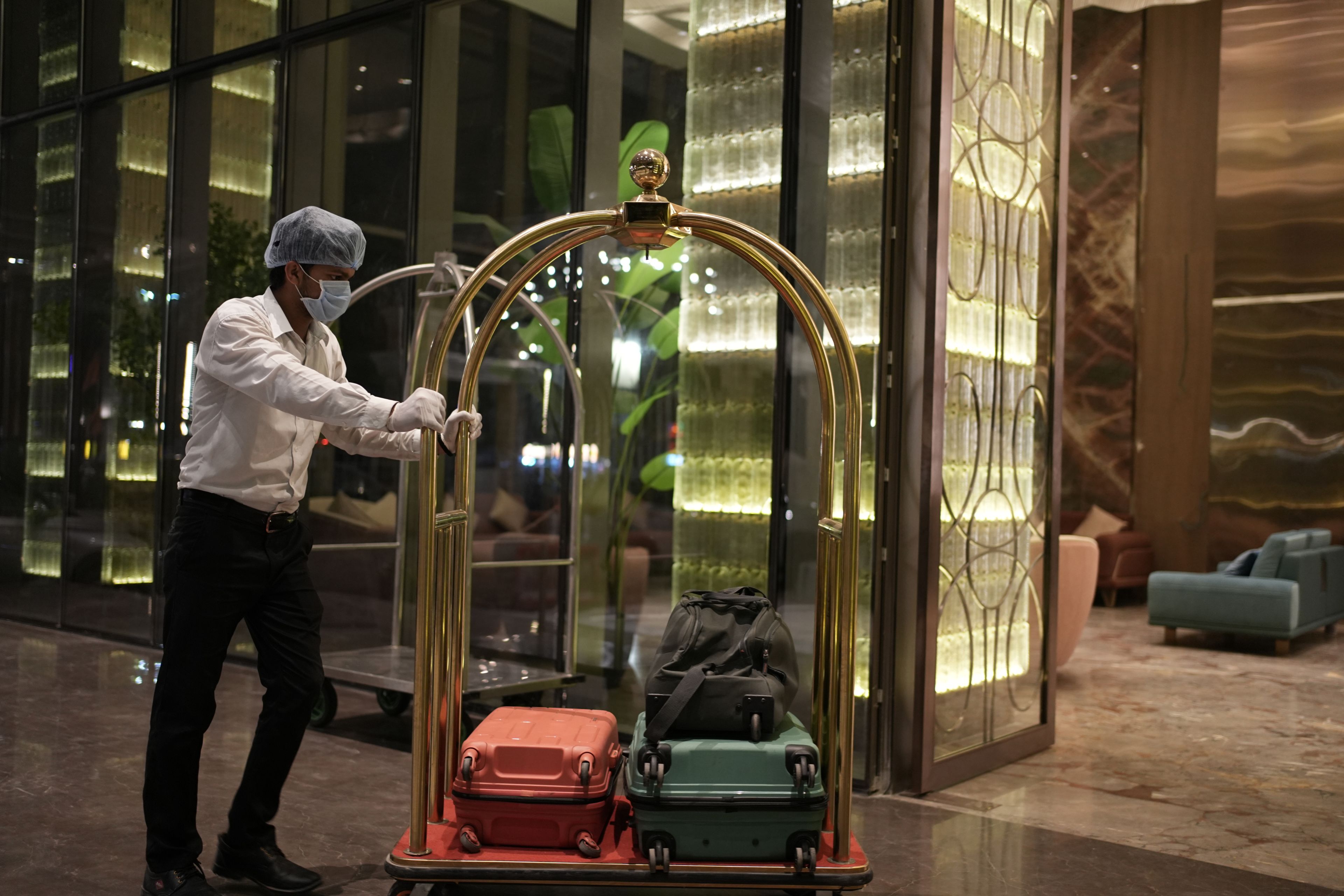 A person pushing a luggage cart with two suitcases through a hotel lobby with glass doors and a modern interior design.