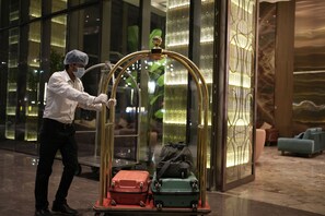 A person pushing a luggage cart with two suitcases through a hotel lobby with glass doors and a modern interior design. - MEGHDOOT RESORT PRIME (Ujjain)