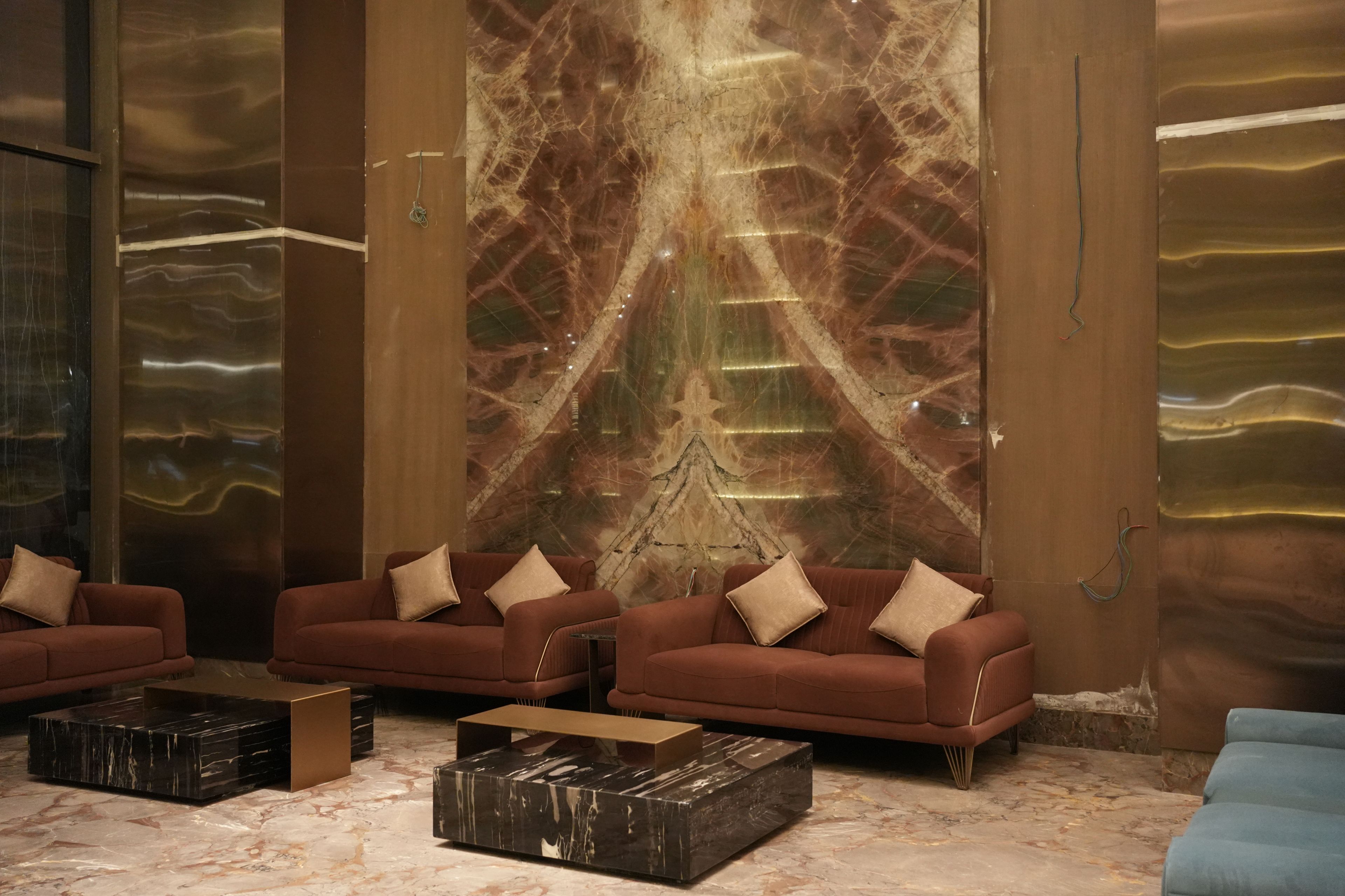 Un vestíbulo con piso de mármol, una pared grande con diseño geométrico y tres sofás con cojines.