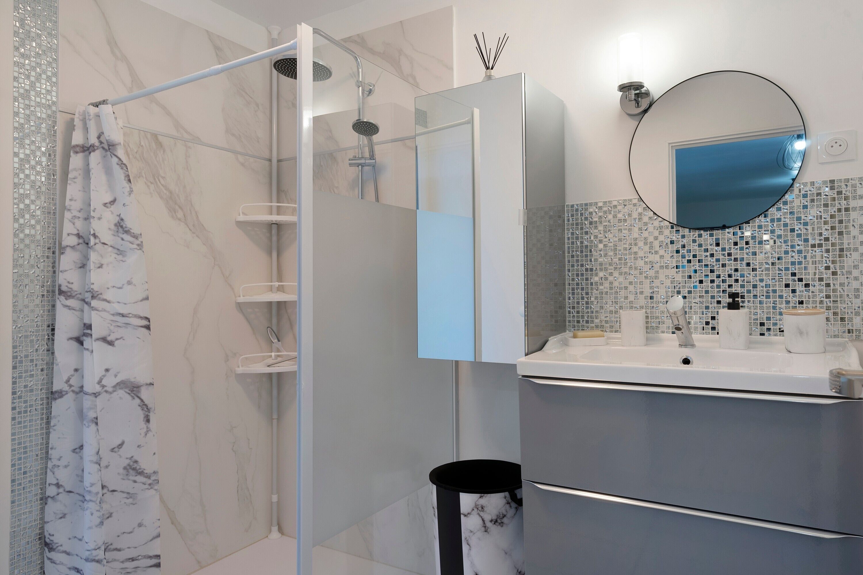 Un bagno moderno con cabina doccia in vetro, parete rivestita in marmo, lavandino con specchio e schienale piastrellato.