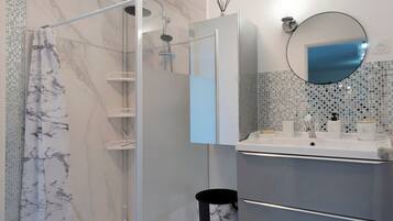 Un bagno moderno con cabina doccia in vetro, parete rivestita in marmo, lavandino con specchio e schienale piastrellato.