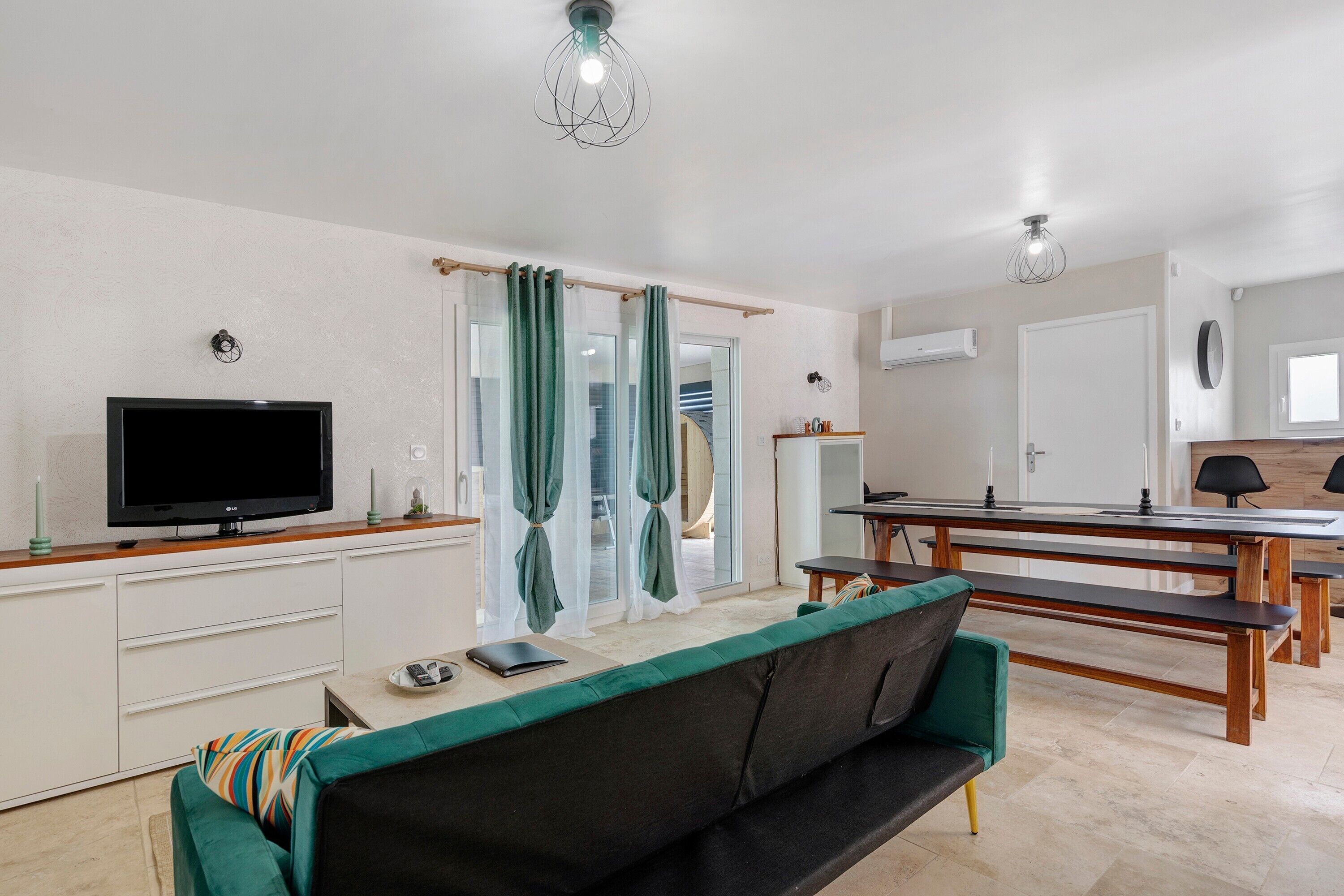 Ein modernes Wohnzimmer mit Flachbildfernseher, einer Couch, einem Esstisch und einer Bank.