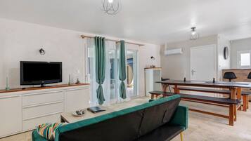 Ein modernes Wohnzimmer mit Flachbildfernseher, einer Couch, einem Esstisch und einer Bank.