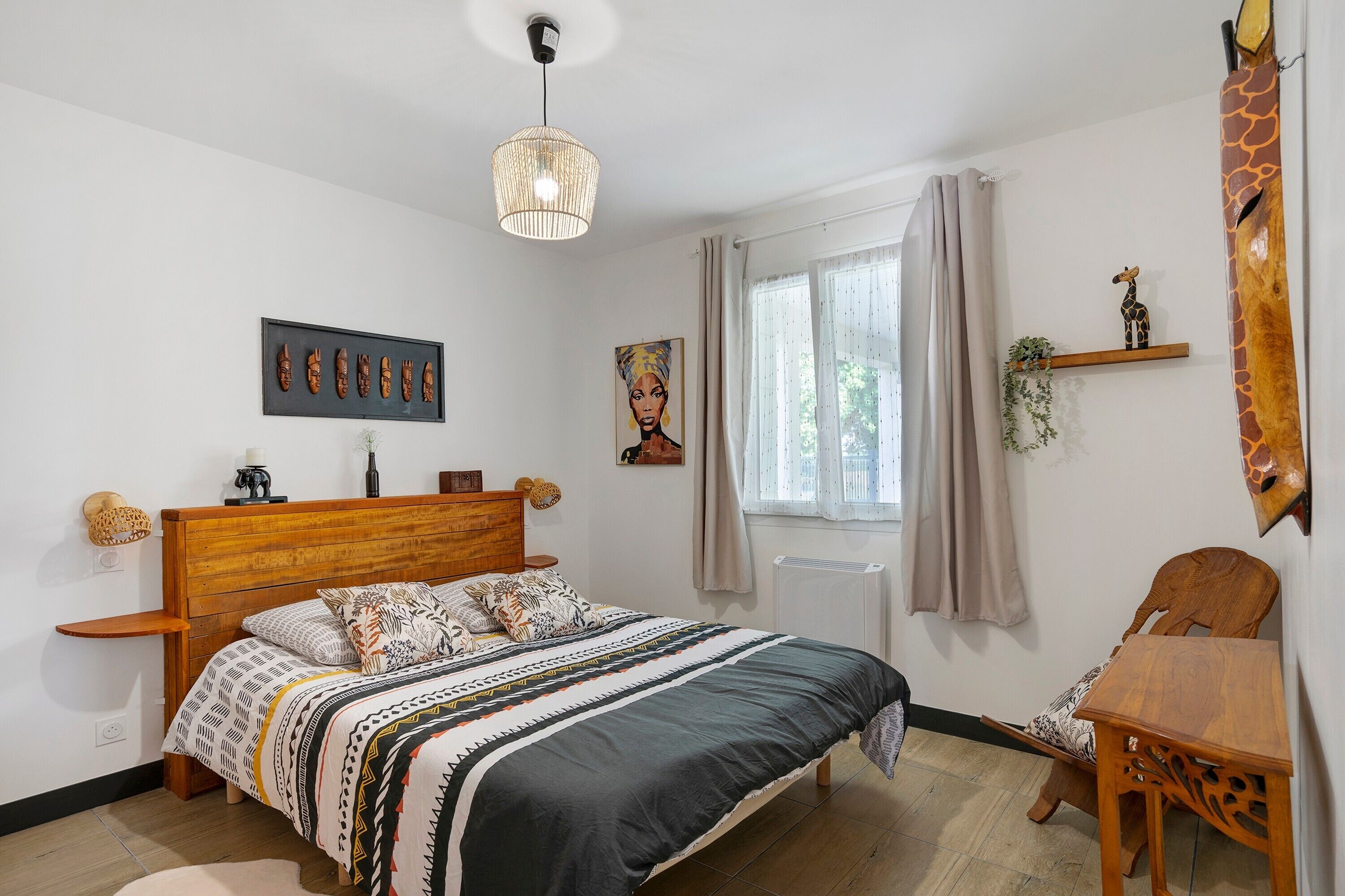 Une chambre avec un lit en bois, un luminaire suspendu, une fenêtre avec des rideaux et une sculpture de girafe accrochée au mur.