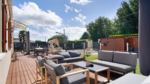 Una terraza de madera con mobiliario exterior, incluyendo sofás y sillones, y un espacio cubierto con techo curvo.