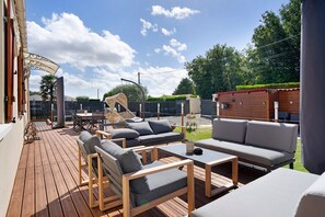 A wooden deck with outdoor furniture, including sofas and chairs, and a covered area with a curved roof.