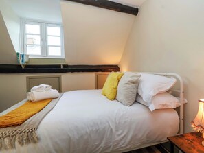 Ein Schlafzimmer mit einem Bett, Kissen, einem gefalteten Handtuch, einem Nachttisch mit Lampe und einem Fenster mit Büchern auf der Fensterbank.
