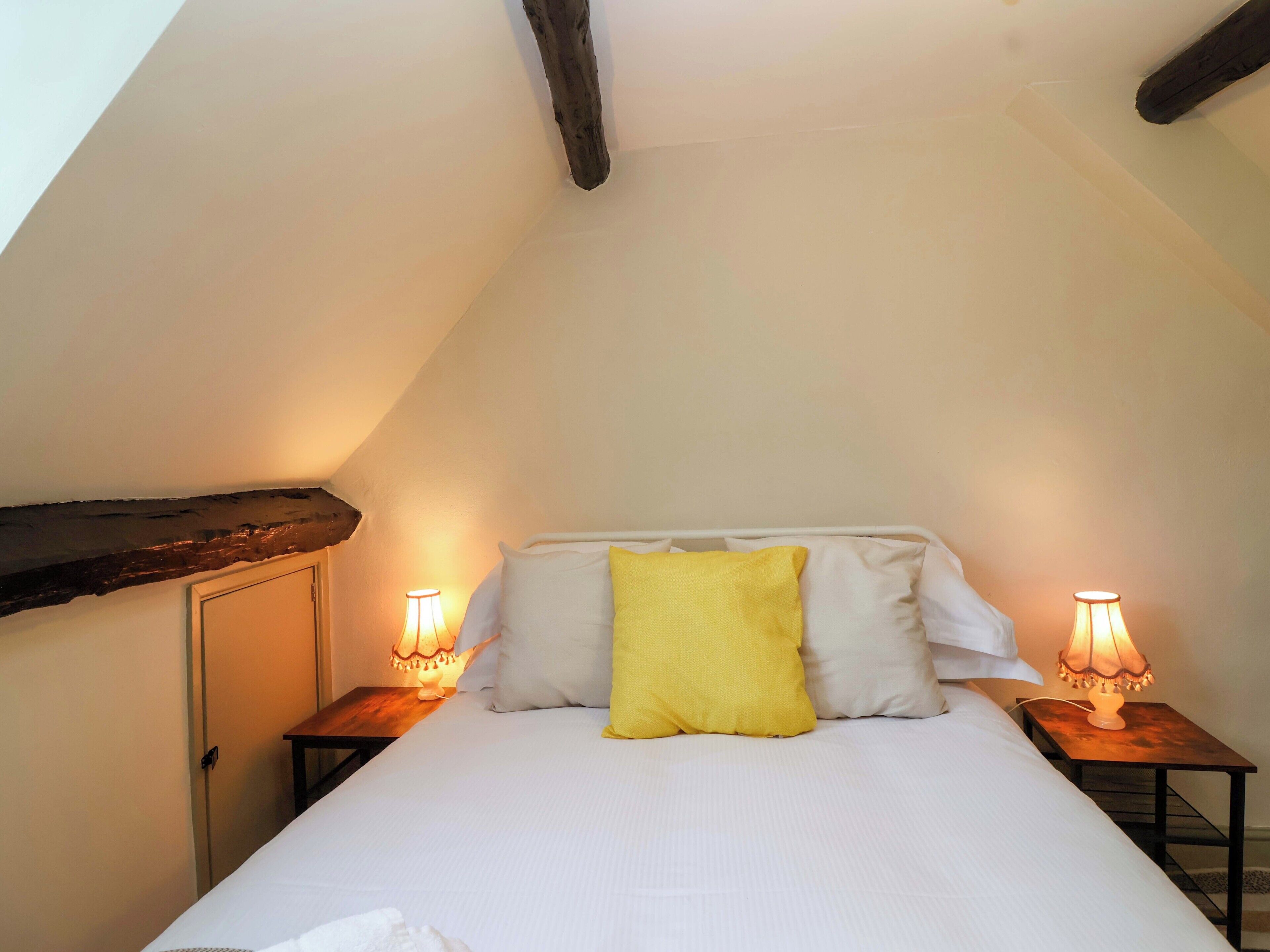 Ein Schlafzimmer mit einem Bett, zwei Nachttischlampen und einer Holzbalkendecke.