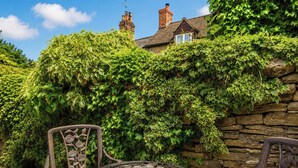A garden with a stone wall covered in ivy, a metal table with intricate designs, and two metal chairs with floral patterns. - 29 Spring Street (Chipping Norton)