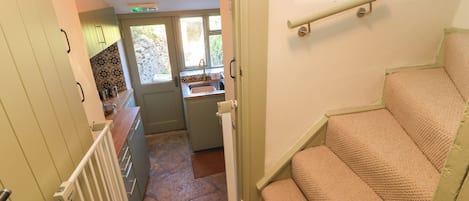 Una escalera conduce a una cocina con suelo de piedra, una ventana y una lámpara en el techo.