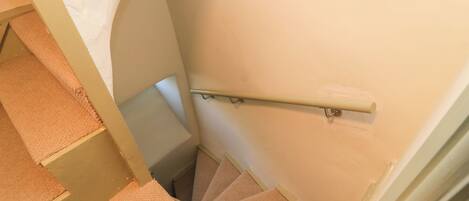 Un escalier en colimaçon, avec des marches recouvertes de moquette et une rampe, menant à l’étage supérieur.