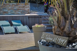A wooden deck with lounge chairs, a potted plant with a sign, and a palm tree.