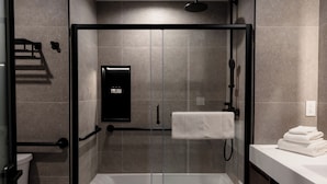 A modern bathroom with a glass-enclosed shower, a white bathtub, and a sink with a towel stack.