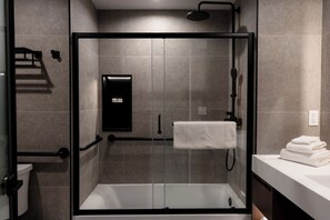 Un baño moderno con ducha de vidrio, bañera blanca y lavamanos con una pila de toallas.
