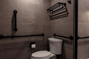 A bathroom with a white toilet, grab bars, a towel rack, and a toilet paper holder.