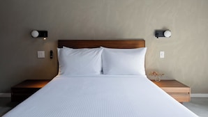 A neatly made bed with white linens, a wooden headboard, and two bedside tables with wall-mounted lamps.
