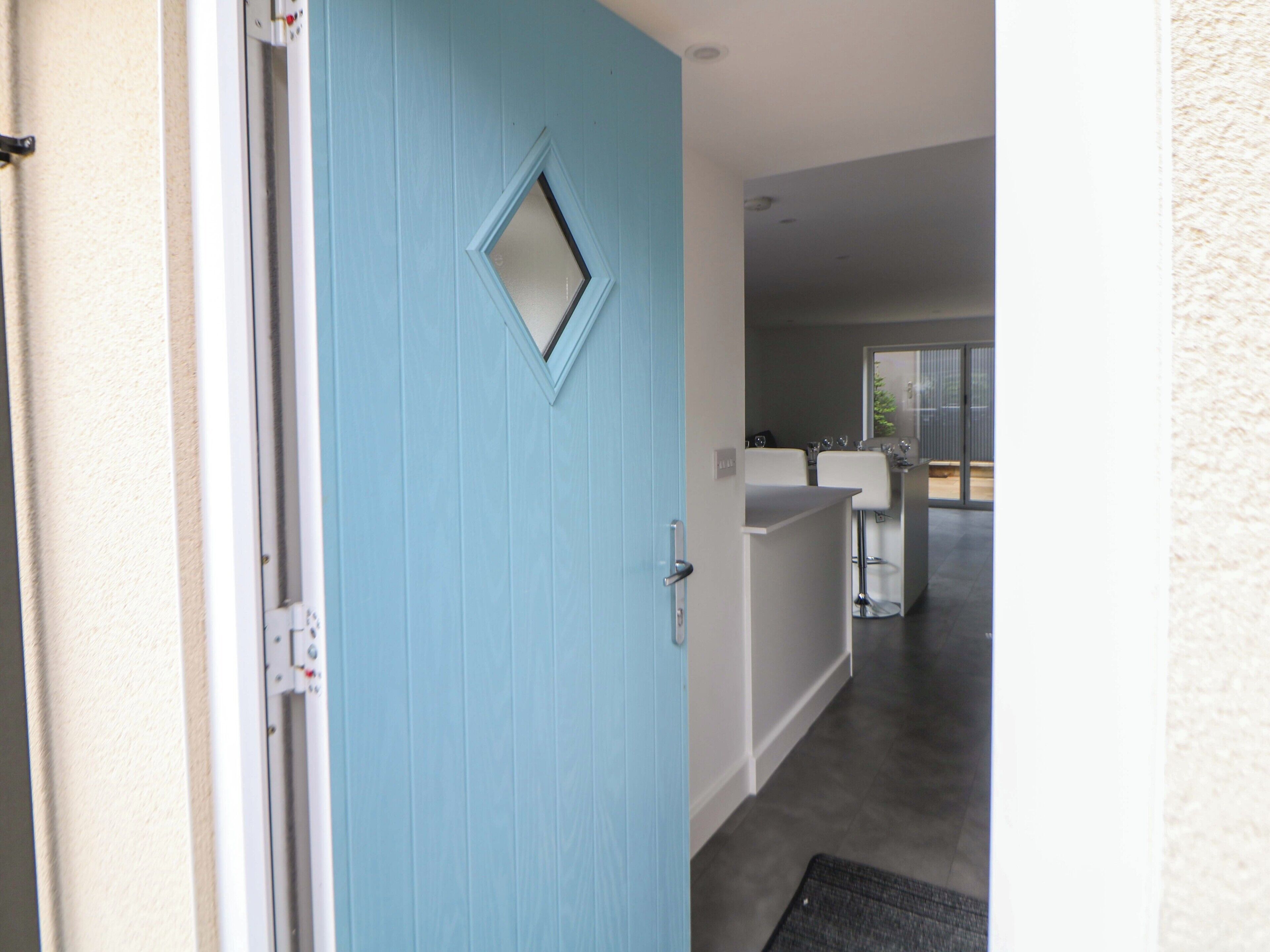 A hallway leading to a kitchen area with a blue door, a small window, and a view of the outdoors.