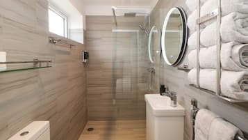 A modern bathroom with a glass-enclosed shower, a toilet, a sink, and a towel rack with neatly folded towels.