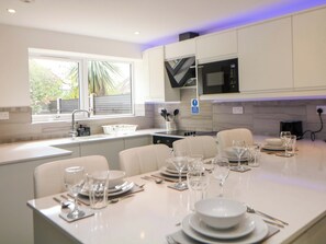 A modern kitchen with white cabinetry, a built-in microwave, and a dining area set for six with white tableware. - Baytree House (Sheffield)