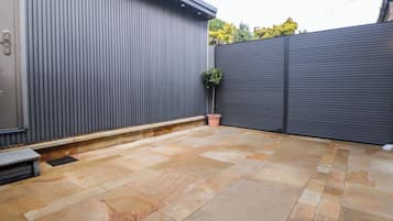 A patio area with stone flooring, a metal fence, and a potted plant.
